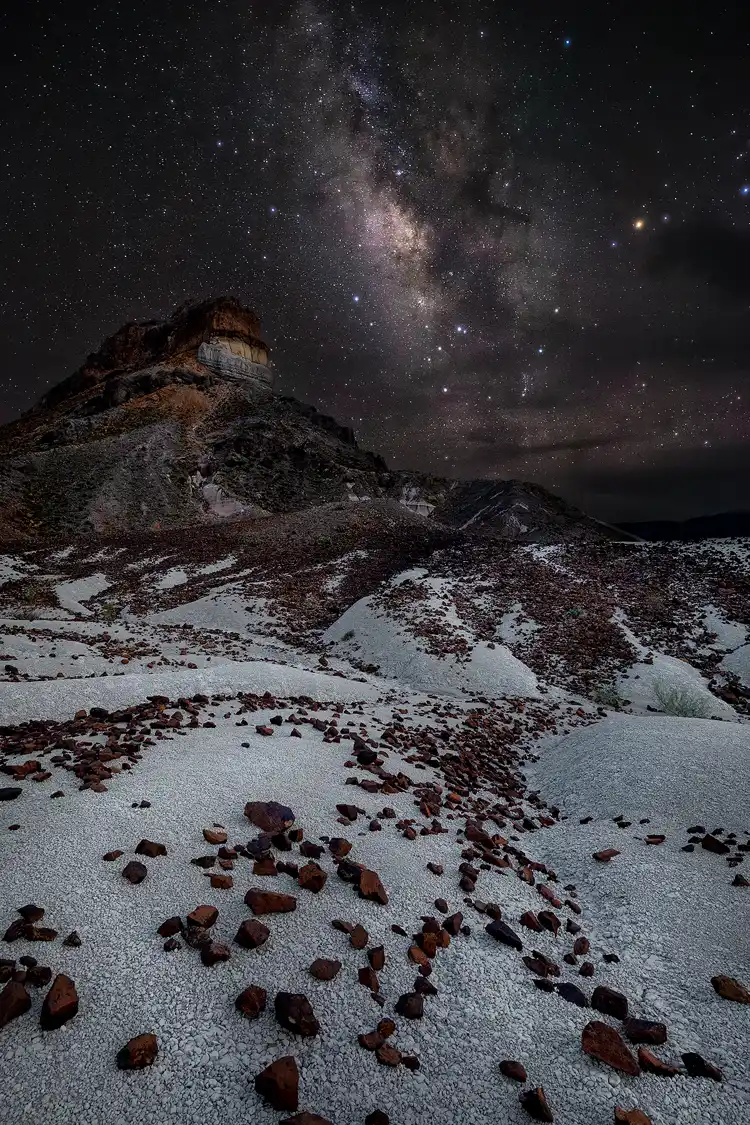 Photography location; Leading lines seem to arise from hillside drainage patterns in this stark desert landscape. In the bottom of this vertical image white ash soil strewn over with reddish rocks bring the eye into the scene and back to the mid-ground half way up the frame. Here, Cerro Castellan rises into the night sky on the left side, while the bright core of the Milky Way occupies the right.