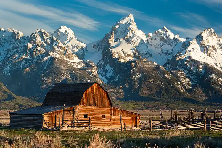 Photography location; First light splashes across the snow laden Grand Teton mountains rising dramatically above the north Moulton Barn, whose structure mimics the shape of the mountains.