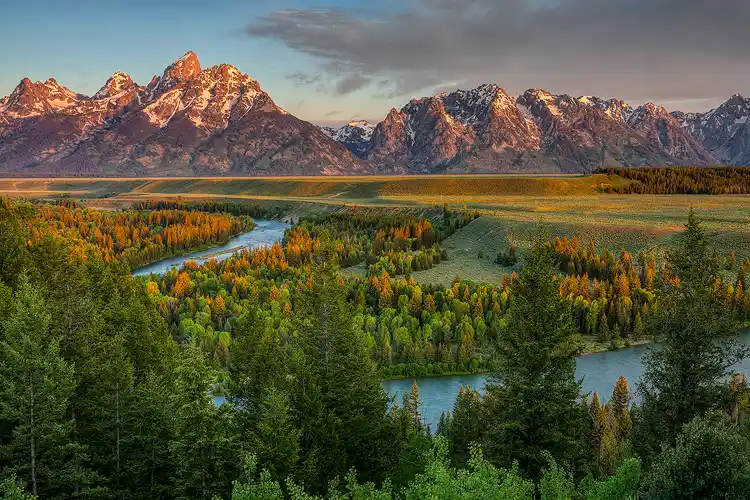 Workshop location; Sunrise panorama from Snake River Overlook. The Snake River winds through the scene as morning light skitters across the tops of mid-ground trees and gently glows on the Grand Teton mountains.
