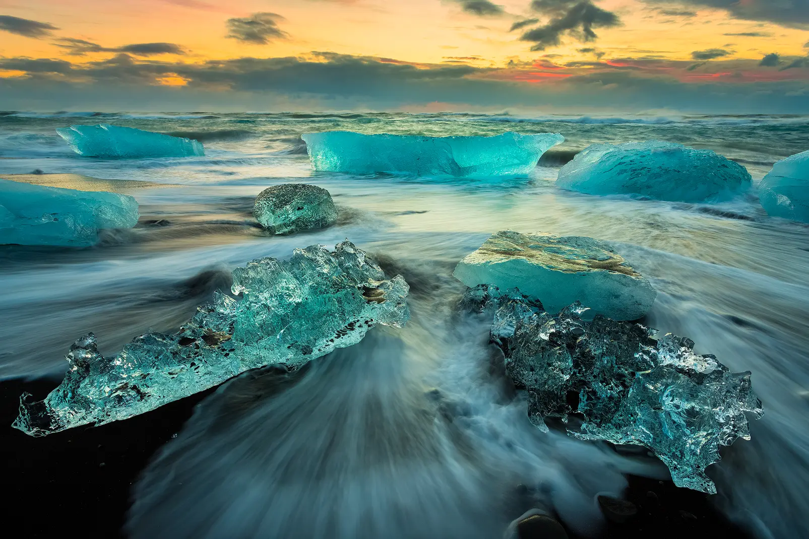 Iceland black sand beach sunrise photograph: glacial ice chunks, aqua-colored, on volcanic sand. Photo by Andy Cook.