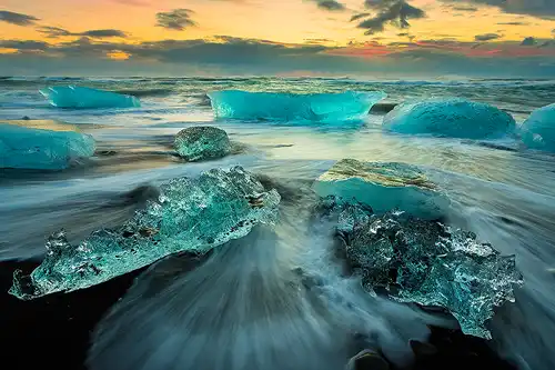 Sunrise photo of blue-green glacial ice on a black sand beach in South Iceland.