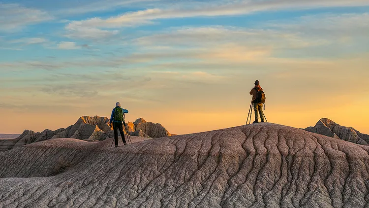Two photographers standing on a barren hill photographing sunset in Badlands.