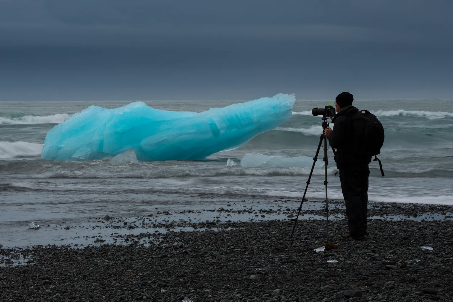 A photographer photographing glacial ice on a black beach.