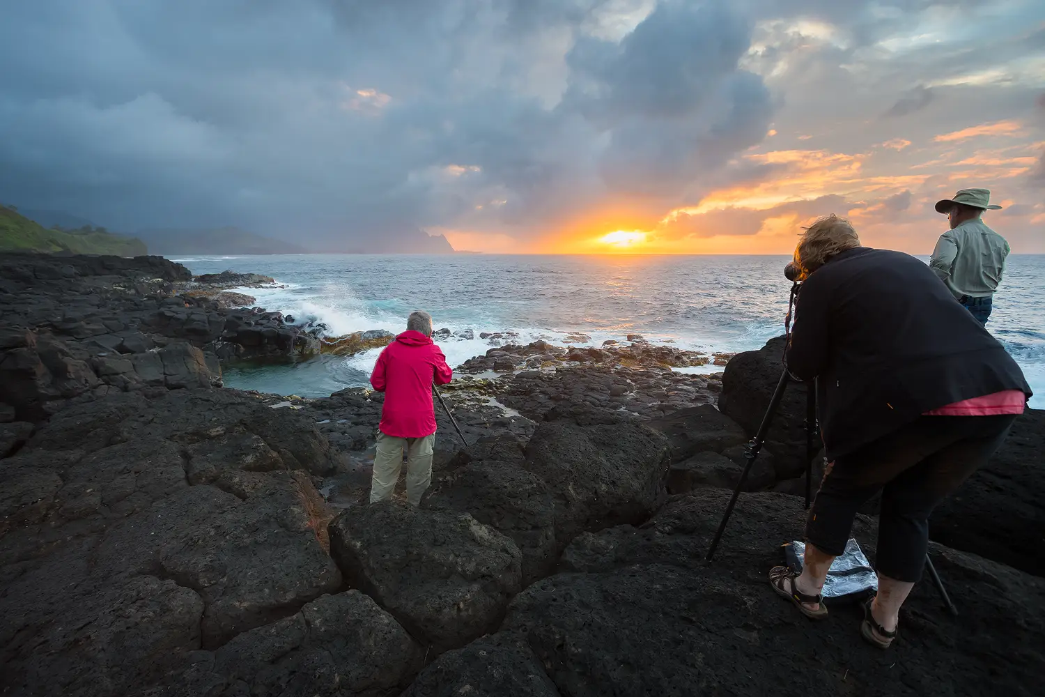 Workshop participants photographing a dramatic sunset on the rocky shore in Kauai.