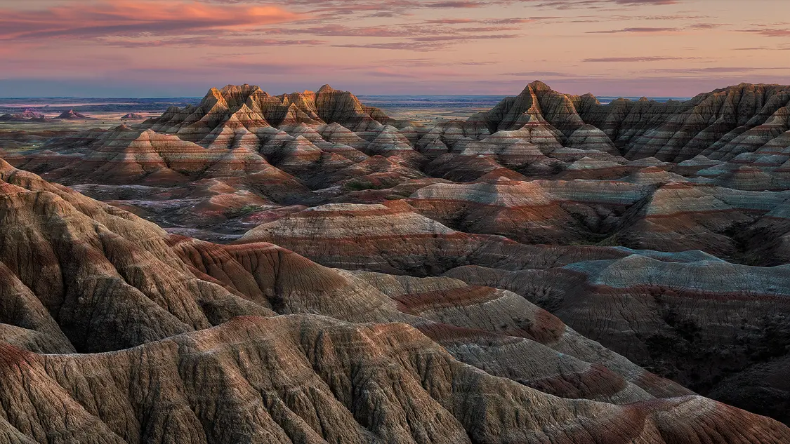 Layered Badlands formations stretching toward the horizon beneath a colorful sunset sky in Badlands National Park.