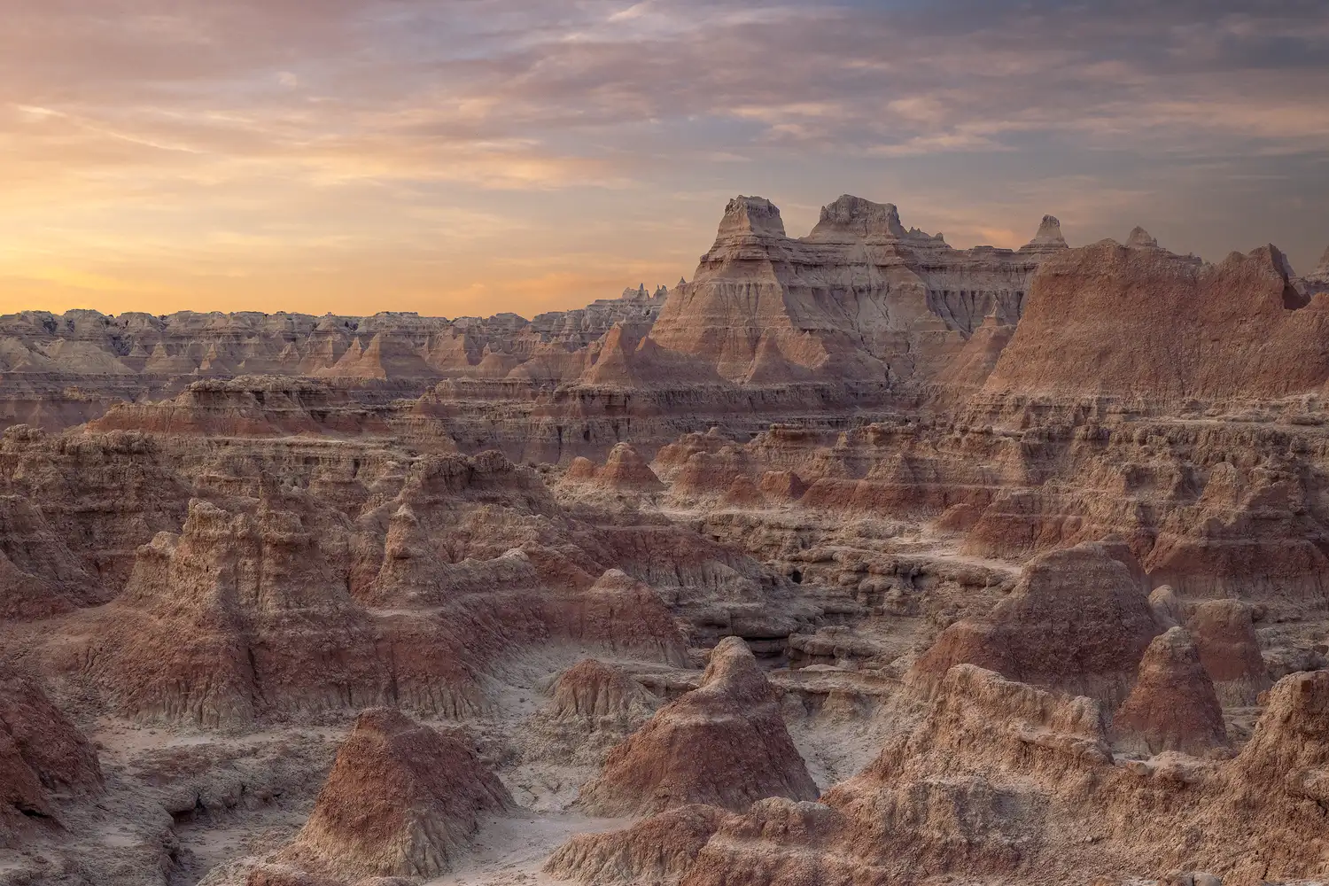 Stratified clouds and haze over conical, layered mounds in Badlands National Park at dawn.