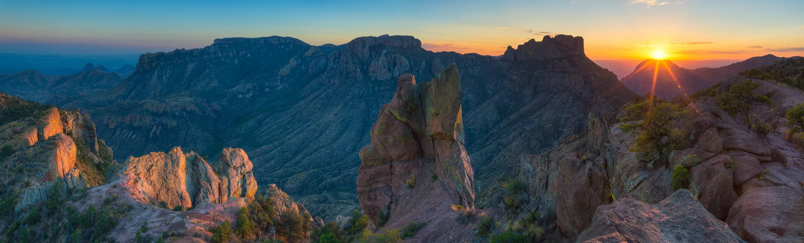Sunset panorama from Lost Mine Trail in Big Bend National Park, showing jagged cliffs, a deep valley, and vibrant sunset color.