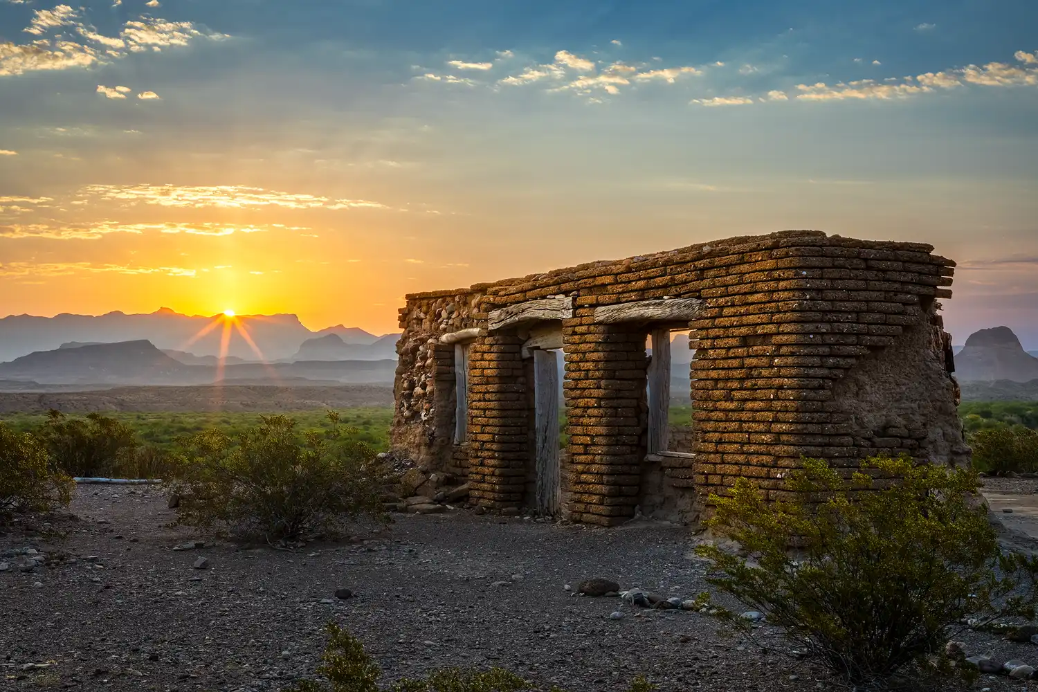 Sunrise sunstar illuminating adobe ruins along the Dorgan Sublett Trail in Big Bend National Park, with the Chisos Mountains in the background.