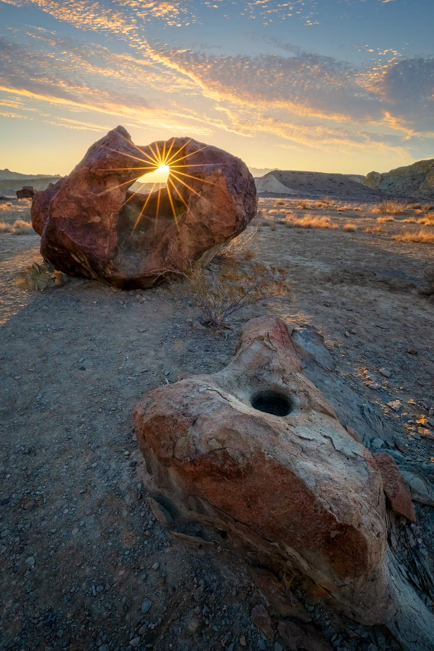 Sunrise sunstar through a donut-shaped rock in Big Bend National Park, with a Native American grinding hole in the foreground.