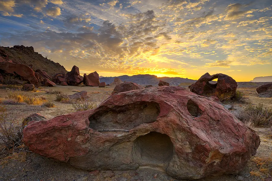 Weathered volcanic boulder with sculpted cavities at Indian Head in Big Bend National Park, illuminated by a colorful sunrise.