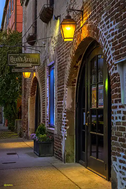 Warm lanterns lighting the brick storefronts along Queen Street in Charleston.