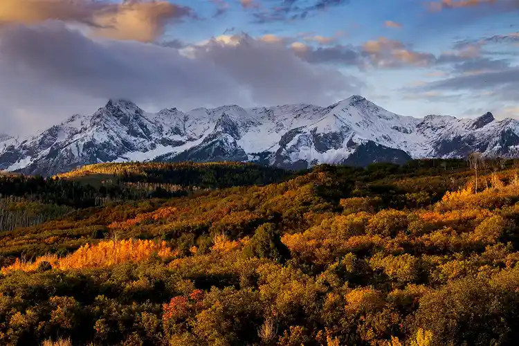Fresh snow on the San Juan Mountains above colorful autumn forests from Dallas Divide, Colorado.