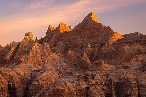 Sunrise view of dramatic peaks from Norbeck Pass, Badlands National Park, with golden light illuminating the landscape and colorful clouds in the sky. Photo by Cindy Beckett.