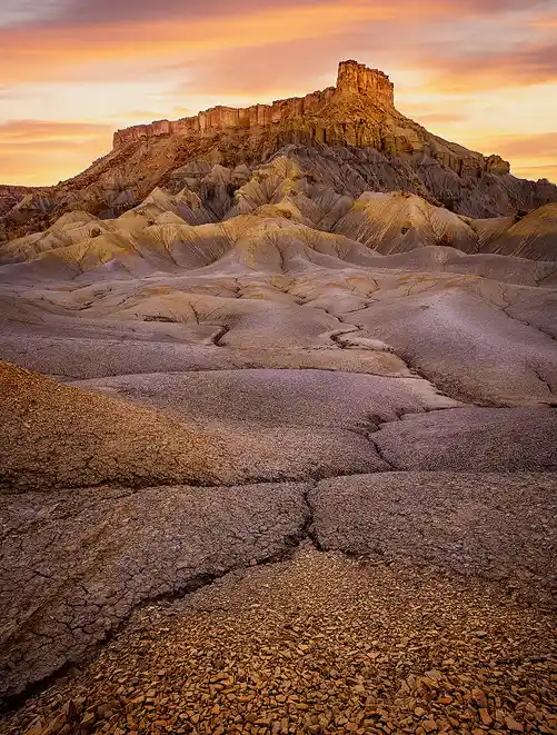 Cracked badlands leading to North Caineville Mesa glowing in sunset light near Hanksville, Utah.