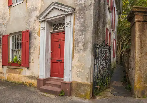 Historic home, red shutters, Charleston. Mottled exterior, gated path. Morning light. Photo by Rick Thompson.