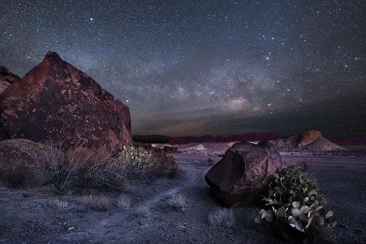 Milky Way rising over the desert landscape at Indian Head, Big Bend National Park, with large boulders, cactus, and starry night sky. Photo by Mike Basista.