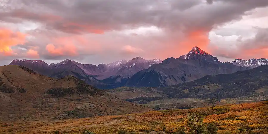 Sunset light on Mount Sneffels beneath glowing pink clouds in the San Juan Mountains of Colorado.