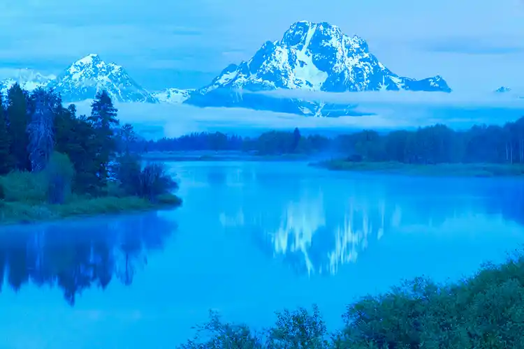 Mount Moran reflected in the Snake River at Oxbow Bend beneath a band of morning fog, Grand Teton National Park.