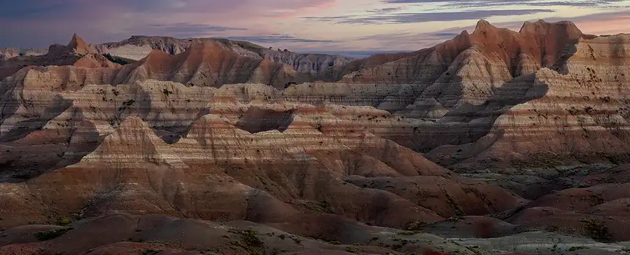 First light of dawn brushing the layered ridges above shadowed valleys in Badlands National Park.