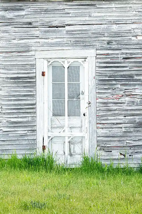 Weathered white screen door set into aged clapboard siding in Port Clyde, Maine.
