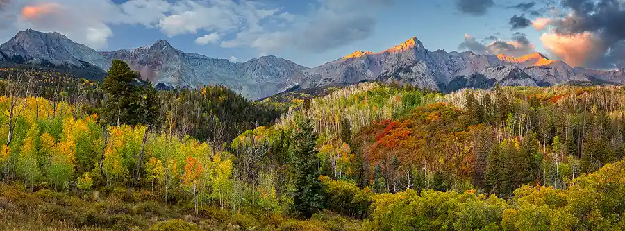 First light illuminating the highest peaks above colorful autumn forests in the San Juan Mountains of Colorado.