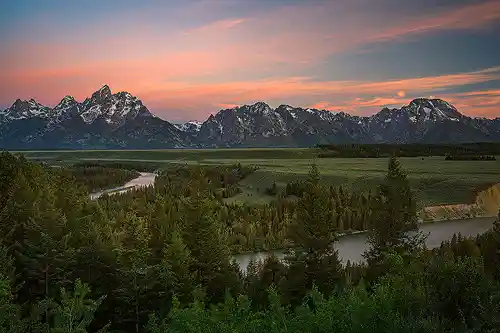 Morning Light Over Snake River Morning photo from Snake River Overlook in Grand Teton National Park with snow-capped peaks, glowing clouds, and the Snake River winding through evergreen forest. Image by Mark Leatherman.
