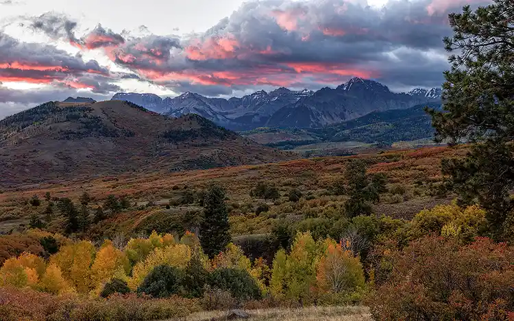 Pink sunrise clouds above Mount Sneffels and colorful autumn valleys in the San Juan Mountains of Colorado.