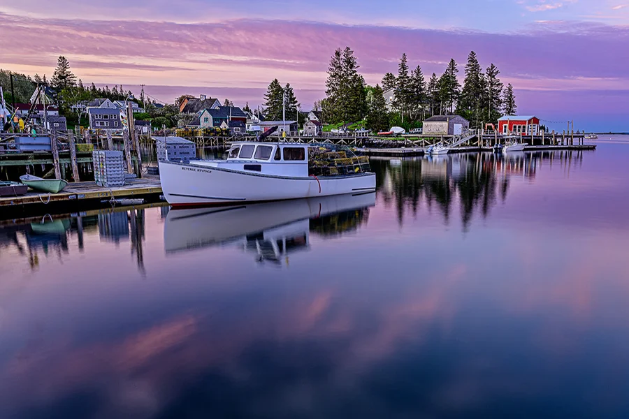 Lobster boat reflected in the calm harbor at sunrise in Port Clyde, Maine.