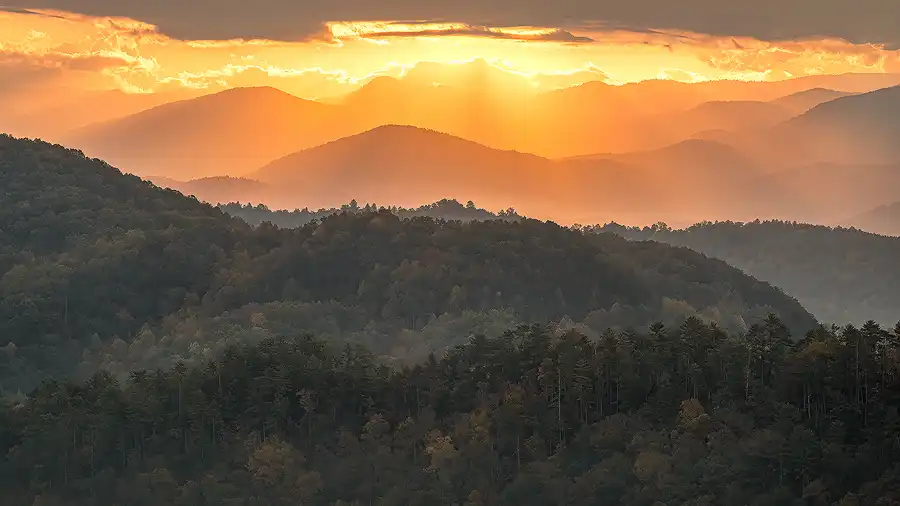 Morning sunbeams break through clouds, illuminating layered mountain ridges from Foothills Parkway in Great Smoky Mountains National Park.
