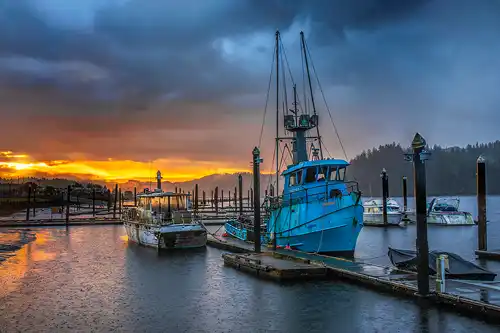 Stormy sunrise over Florence Harbor, Oregon Coast. Fishing boats and piers. Photo by Harriet Feagin.