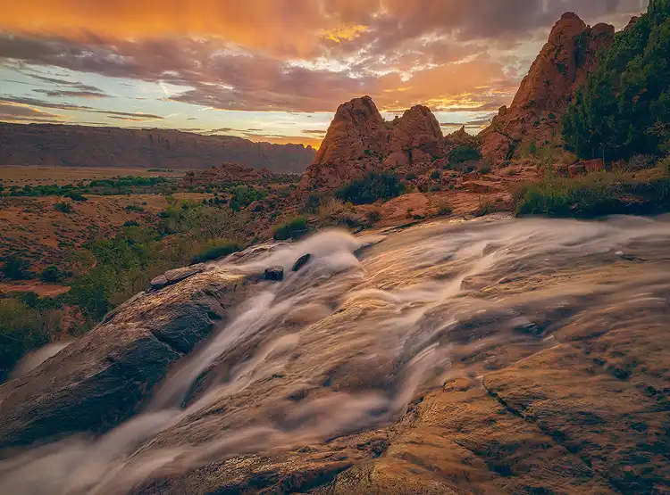 Water flowing over slickrock beneath glowing sunset skies at Faux Falls near Moab, Utah.