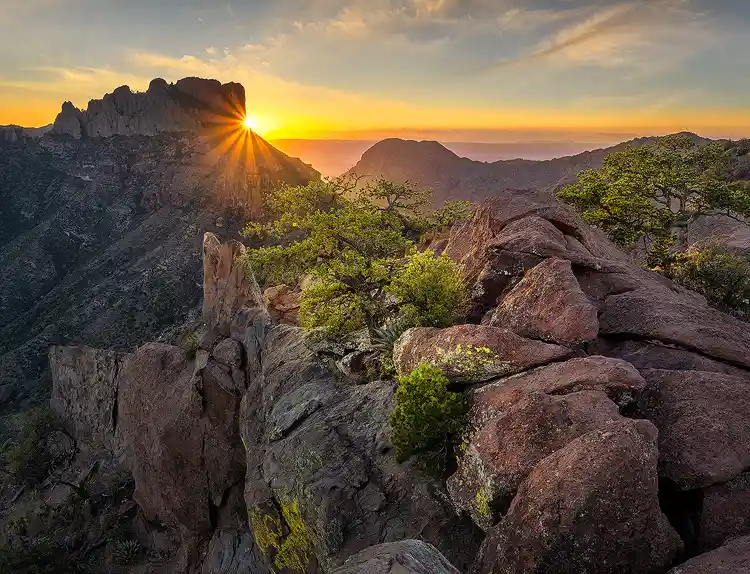 Rocky summit along Lost Mine Trail leading toward a sunset sunstar over the Chisos Mountains in Big Bend National Park.