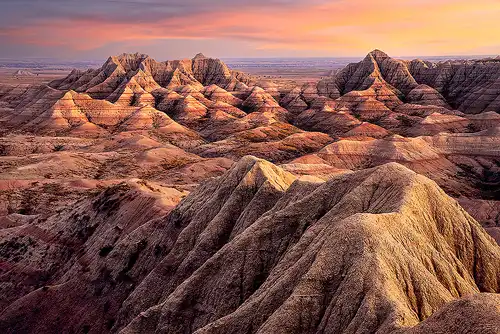 Badlands National Park at sunset, with late evening side light illuminating eroded hills and canyons, distant mountains, and a colorful sky. Photo by Cindy Beckett.