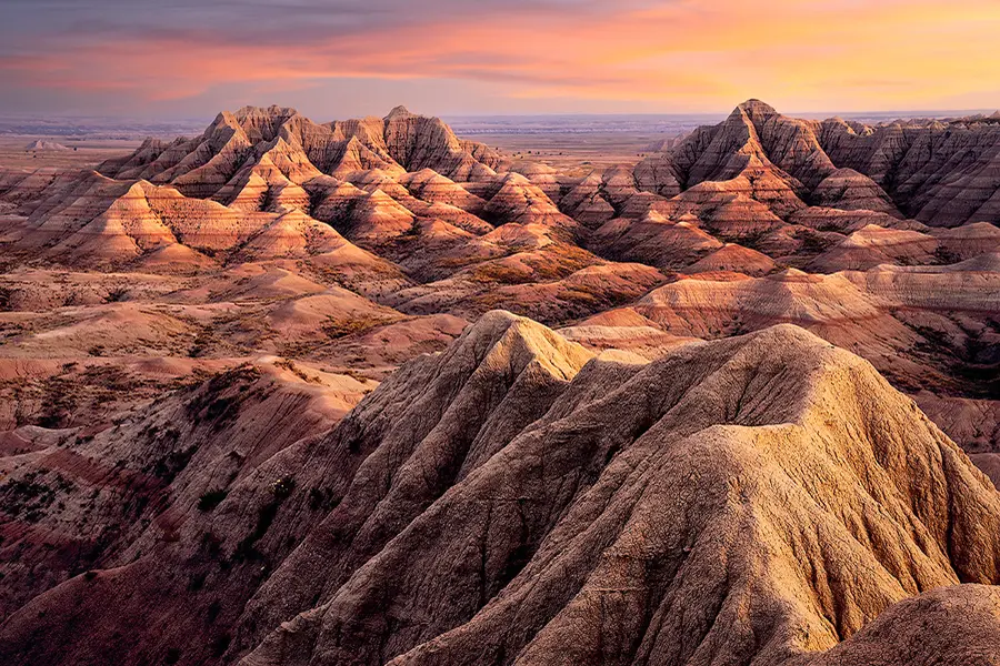 Sunset light sweeping across layered ridges and buttes in Badlands National Park.