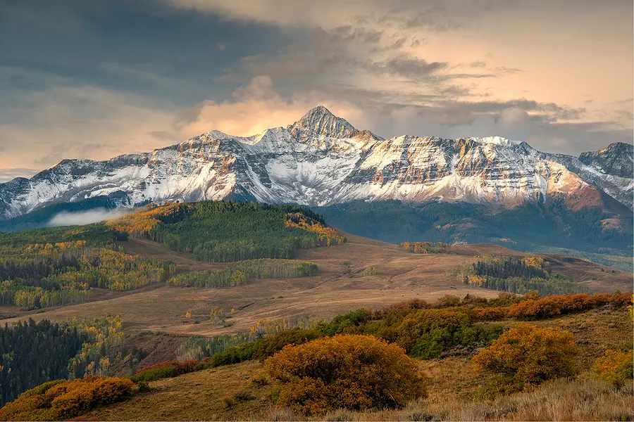 Wilson Peak illuminated by sunrise above autumn hillsides and golden aspens along Last Dollar Road in Colorado.