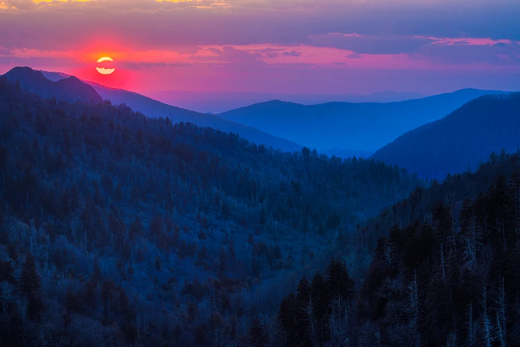 Sunset over the Smoky Mountains in spring, with layered blue ridges and a red sky.