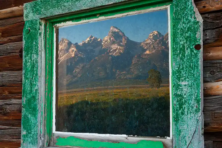 Grand Teton mountains reflected in a cabin window.